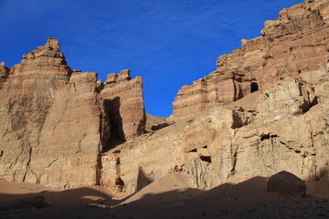 Flat relief walls and rocks of the sandy-clay canyon Charyn against the sky with clouds, sunny