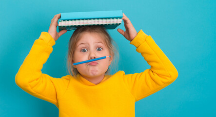 Naughty little girl holding a pencil like a mustache between lips and nose and books on her head on blue background. Concept of education.