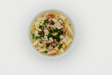 Chicken soup in a bowl with noodles, fresh vegetables and chicken meat photographed from above on a white background