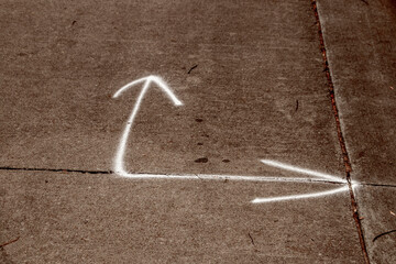 Two pointed bent arrow painted in white on dark grungy textured cement sidewalk or road.