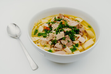 Chicken soup in a bowl with noodles, fresh vegetables and chicken meat photographed from above on a white background and spoon