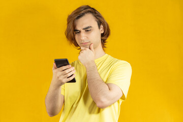 Young man Prep Student with long hair. 20s guy with smartphone on a yellow background