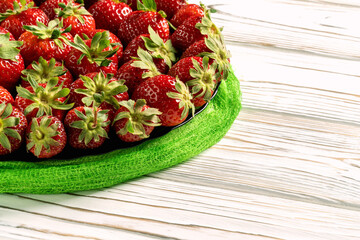Juicy strawberries lie in a glass plate on a wooden background.