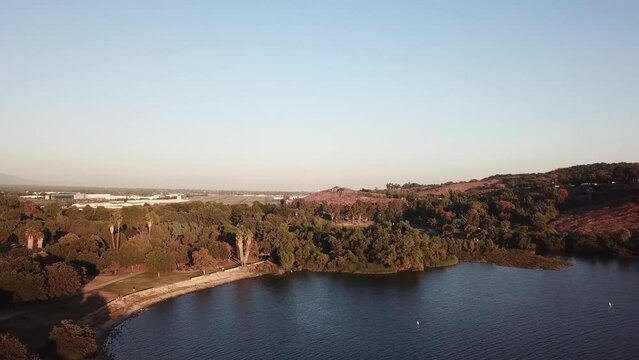 gorgeous footage of a vast rippling blue lake at sunset surrounded by majestic mountain ranges covered in lush green trees and plants with blue sky at Puddingstone Lake in San Dimas California USA