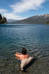 Fototapeta premium young man from behind sitting in the water of a lake with transparent waters with a landscape of mountains