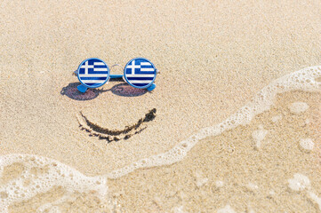 A painted smile on the beach and sunglasses with the flag of Greece. The concept of a positive holiday in the resort of Greece. - obrazy, fototapety, plakaty