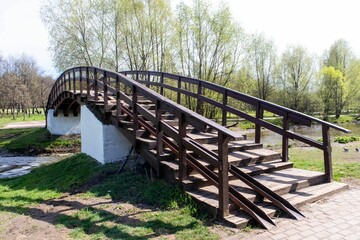 Semicircular wooden bridge with railings across the river. The time of the year is spring. High quality photo.