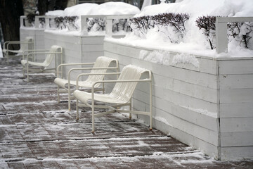 Metal benches on the snow-covered terrace with wooden decking