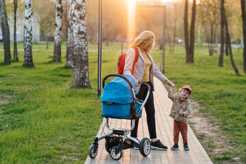 mom walks with stroller and toddler son in the park