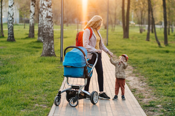 mom walks with stroller and toddler son in the park
