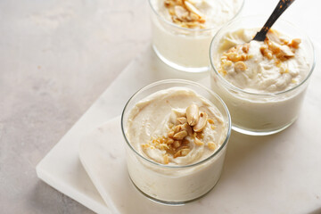 Creamy dairy yoghurt dessert with mascarpone, cream cheese and peanut butter in glasses on marble tray with a tea spoon