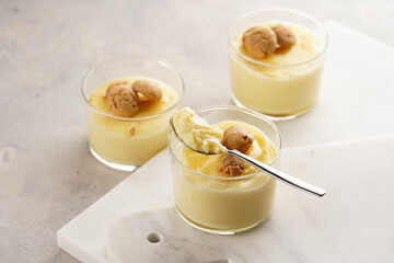 Creamy french vanilla pudding in glass decorated with italian biscuits amaretti on marble board on grey neutral background