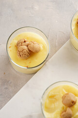 Creamy french vanilla pudding in glass decorated with italian biscuits amaretti on marble board on grey neutral background