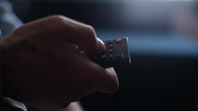 Close-up unrecognizable mature adult male hands holding TV remote control and switches TV channel. Closeup cropped shot of senior man flipping through TV channels with remote control, slow motion.