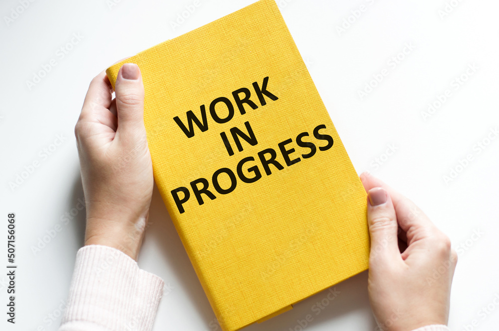 Poster working in progress inscription on a yellow notebook on a white background, a notebook in the hands 