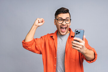 Portrait of a joyful young ukrainian man holding a mobile phone isolated on grey white background, celebrating victory. Happy winner.