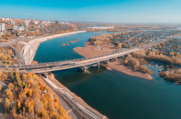 Naklejka premium Aerial cityscape view of city districts with automobile bridge over river in Ufa. Autumn parks with colorful trees