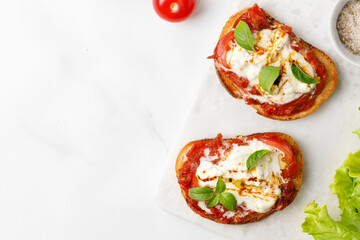 Cheese Bruschettas with stracciatella, tomatoes, basil on marble board, marble background, top view, copy space