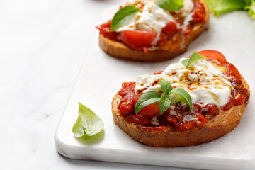 Bruschetta with stracciatella cheese,  tomatoes and basil on marble board. Traditional Italian appetizer, antipasto,  snack.