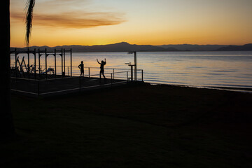 Silhouette of two people doing gymnastics by the sea as the sun sets in Florianopolis in southern Brazil. Boardwalk. Panorama. Nature. Cityscape.