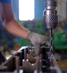 Caucasian technician with gloves working with a vertical drill in a family workshop. Selective focus.