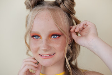 charming blonde tween girl with orange makeup on yellow background. teenager portrait