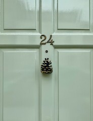 London, England. Door knocker. Pine cone. House number 24 on a pale green wooden front door with a...