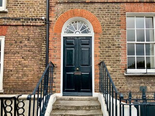 LONDON, UNITED KINGDOM - 07.05.2021. Black wooden door in georgian house in London. Brick wall, stone steps, black metal fence, window and arch above the door. Selective focus