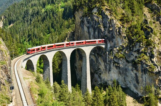 Landwasser viaduct in the Davos mountains near Filisur. Beautiful old stone bridge with a moving train. Spring Time