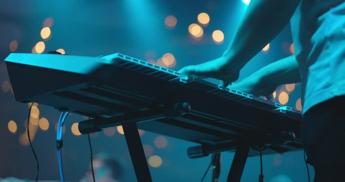 Close up view of musician hand playing synthesizer piano on live concert at stage. The musician playing the electric piano. Blue background