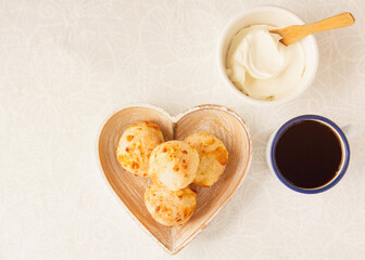 Minas Gerais cheese bread, hot, with a cup of black coffee and cream cheese, on a white tablecloth, copy space, top view