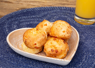 Delicious Minas cheese bread, on a rustic wooden bench, outdoors, with a glass of orange juice