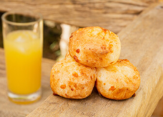 Delicious Minas cheese bread, on a rustic wooden bench, outdoors, with a glass of orange juice in the background