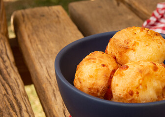 Delicious Minas cheese bread, on a rustic wooden bench, outdoors, with a glass of orange juice