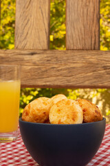 Delicious Minas cheese bread, on a rustic wooden bench, outdoors, with a glass of orange juice, portraiture vertical photo