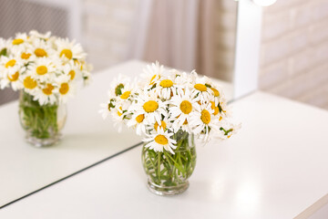 Beautiful chamomile flower bouquet in vase on table in beauty salon, mirror reflection
