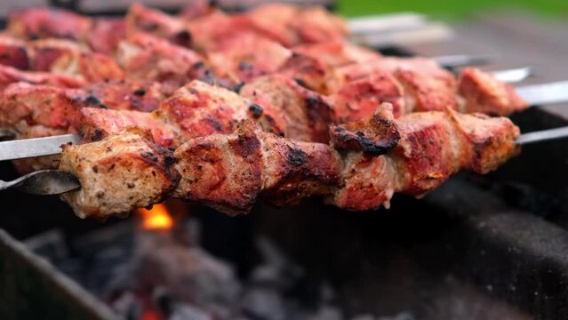 Close-up of grilling tasty dish on barbecue. Process of cooking yummy shashlik in nature. Delicious food on metal skewer in bbq. Time to picnic concept. Street food. Food festival. Pork at the stake