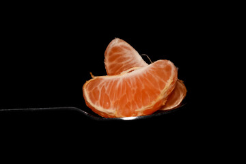 Two orange slices on the spoon on black background.