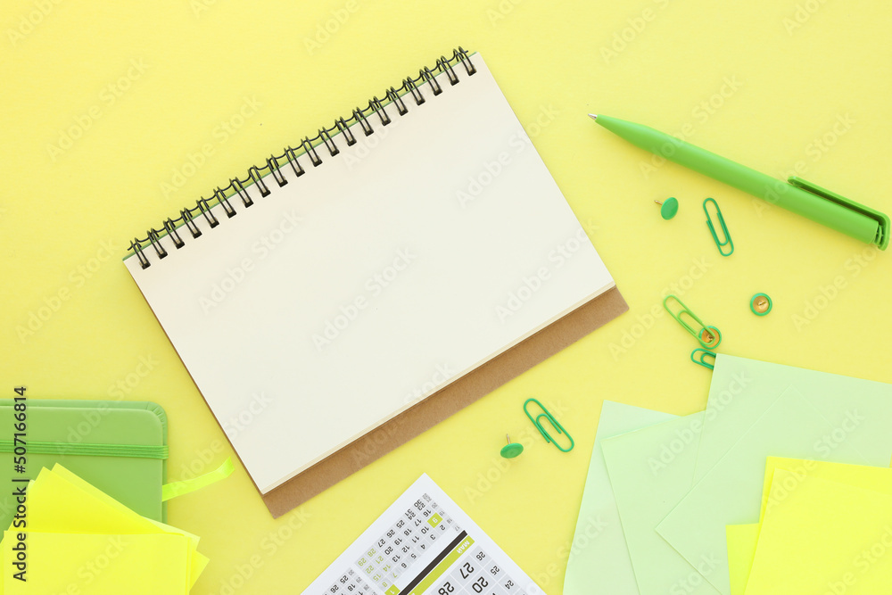 Poster an open notepad with blank white sheets next to yellow sticky notes in a green pen and a green notep