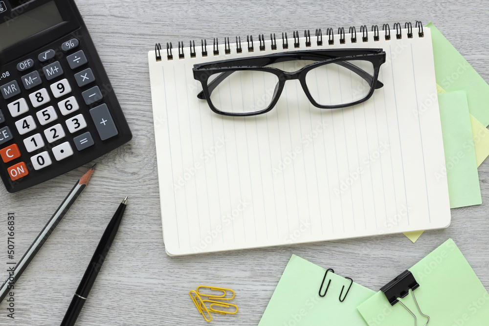 Poster empty notepad, glasses and calculator on a light wooden table at the workplace in the office. top vi