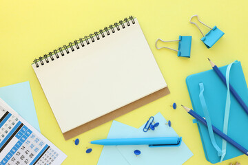 Workspace with notebook mockup, blue notepad clips and stationery calendar on yellow background. Remote work, online learning concept.