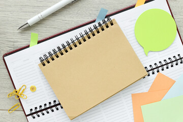 Office equipment such as an open notebook, sticky note, sticky notes and more on a bright wooden office table.