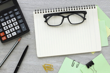 Empty notepad, glasses and calculator on a light wooden table at the workplace in the office. Top view with copy space for your design.