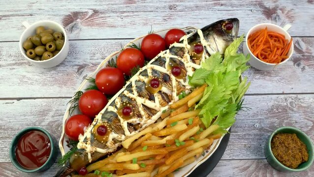 Fried mackerel fish with french fries, tomatoes and celery leaves rotating slowly on turntable.
