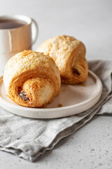 Morning concept. Two fresh croissants on a white plate on a napkin with ea on light background