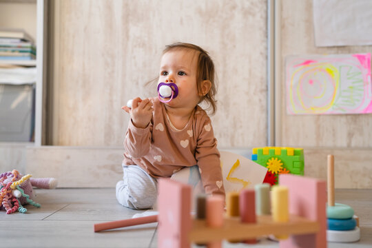 One baby small caucasian infant girl playing on the floor at home copy space holding wooden toys in day front view