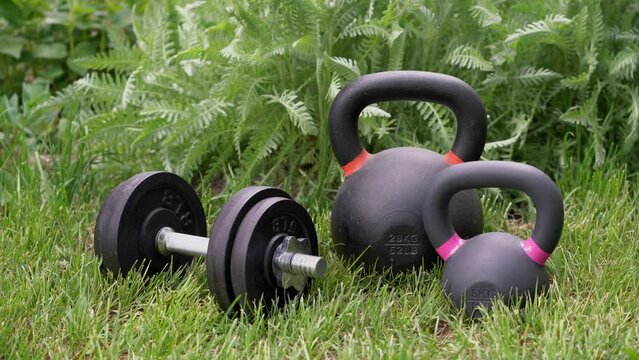 heavy dumbbell and iron kettlebells in backyard with breeze in background leaves, home fitness concept