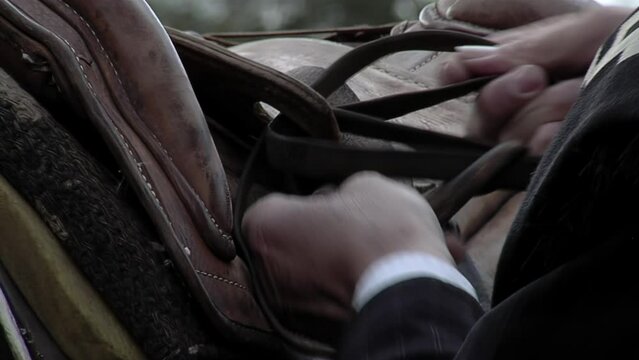Man Hands Putting a Saddle on a Horse. Close Up.