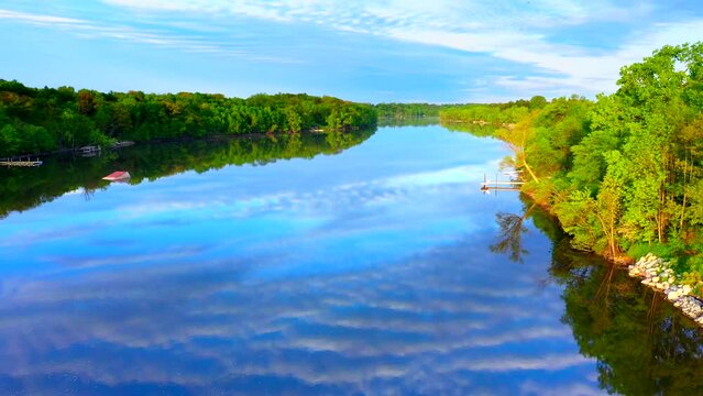 Amazing sky with rippled clouds, mirrored in tranquil river at daybreak, moving aerial view.
