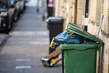 Garbage bins and containers full, overflowing, with bags falling on ground in residential area of...